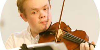 Image depicts Samuel Oliver-Sherry holding a violin and looking at sheet music on a music stand