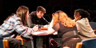 An image of four cast members sat and laughing around a table of the set