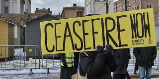 Person holds up yellow sign on which is written 'CEASEFIRE NOW Amnesty International'.