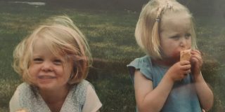 Two young sisters eating ice cream in a field.