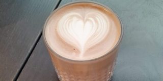 Hot chocolate with a love heart pattern on top, with a cookie by the side on a plate