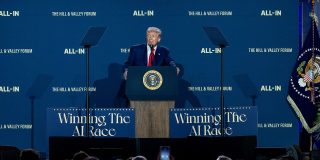 President of the United States Donald Trump stands at a podium with large blue signs on both side saying "Winning the AI Race".